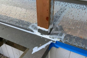 Subfloor railing post nailed to attachment straps and site fabricated flashing protecting post base and tying into adjacent flashing components
